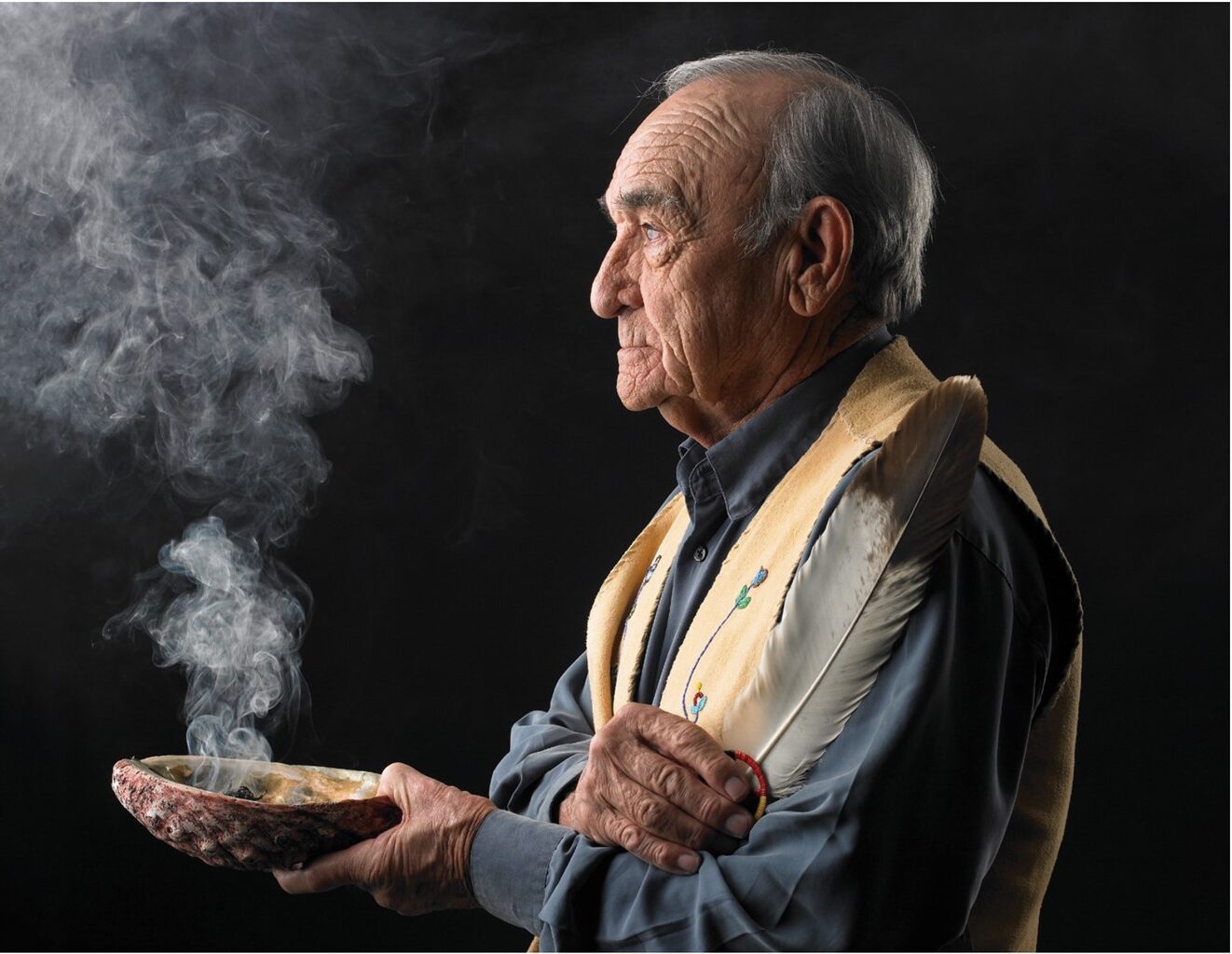 Elderly First Nations man holding a smudging bowl and a feather. 